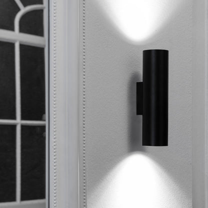Black wall-mounted light fixture on a white wall with a window in the background