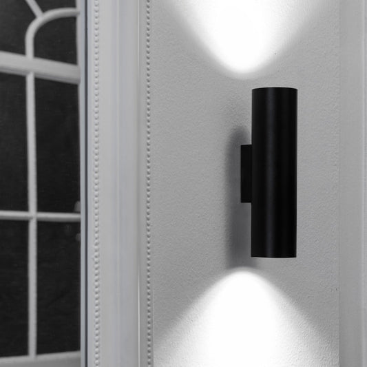 Black wall-mounted light fixture on a white wall with a window in the background
