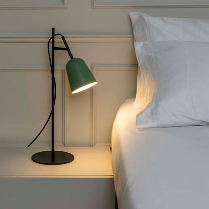 Green lamp on a nightstand next to a bed with white pillows.