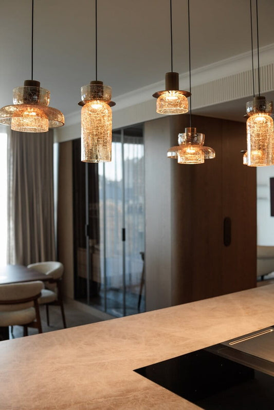 The Signature B modern pendant lights featuring amber glass hanging above a kitchen island counter in a contemporary interior setting. Available to buy at the VXR Space store.