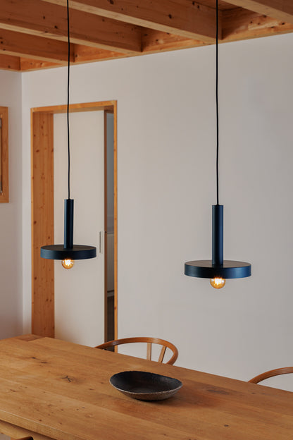 Two hanging pendant lights in a room with wooden ceiling and table.