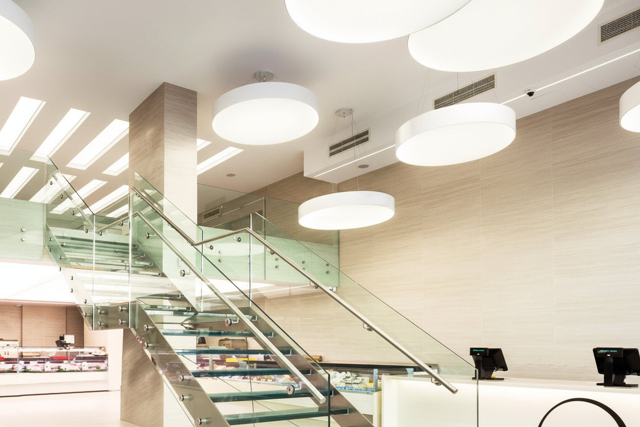 Large circular LED ceiling lights in modern commercial interior with glass staircase architectural lighting