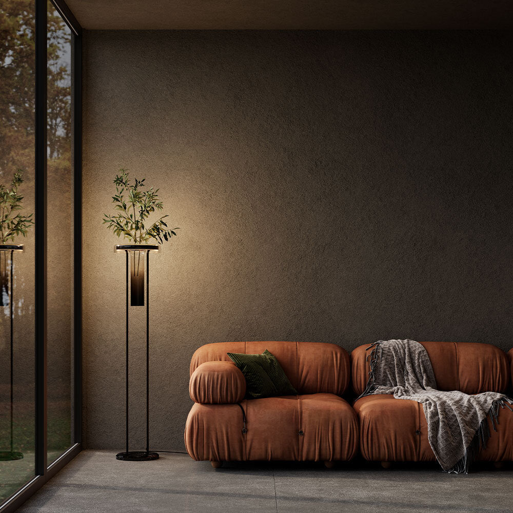 Brown leather sofa with a blanket and green pillow in a modern room with a plant and large window.