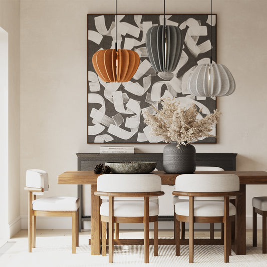 Dining room with wooden table, white chairs, abstract art, and decorative pumpkins.