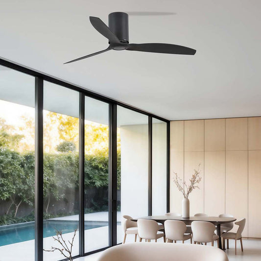 A modern black ceiling fan with three blades installed on a white ceiling in a contemporary living room with large floor-to-ceiling windows, a curved cream sofa, and a black marble coffee table.