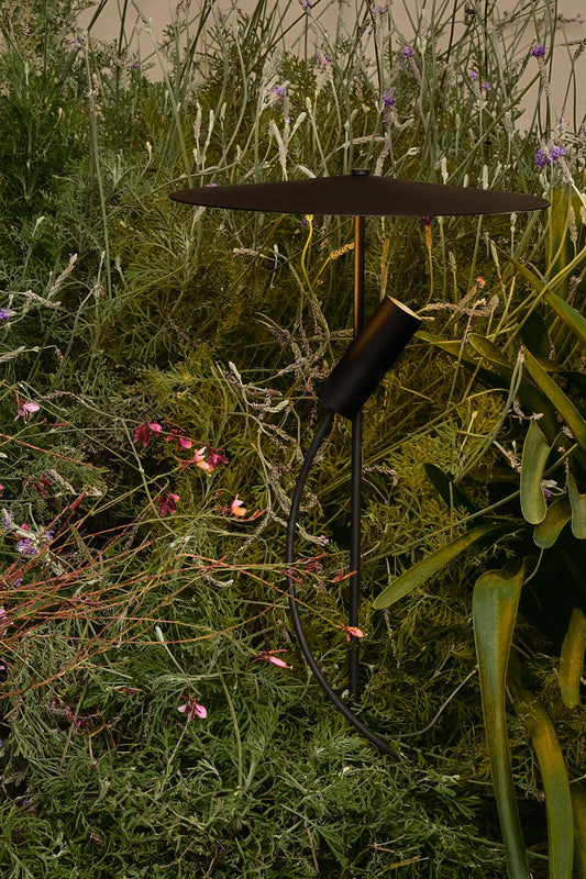 Black outdoor light fixture in a garden setting with greenery and flowers.