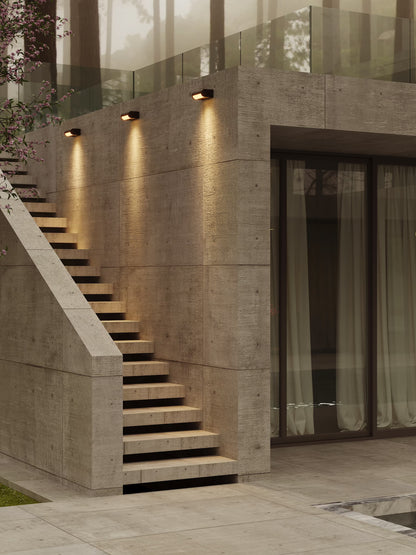 The Solden matte black LED exterior wall sconces mounted on an architectural concrete facade above outdoor stone steps. Available to buy at the VXR Space store.